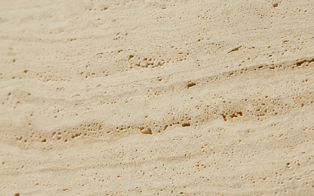 A pale travertine surface with fine pores and subtle sediment layers.
